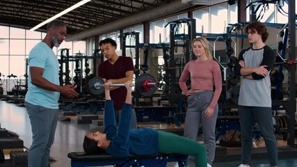 Personal training session in a gym where a group of young individuals learns weightlifting techniques under the guidance of an instructor, focusing on teamwork, encouragement, and skill development. - Powered by Adobe