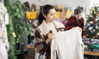Armenian woman examines a sweater before buying it in a clothing store. Woman prepares Christmas gifts and buys warm cozy sweaters. Buying clothes and accessories in the Christmas shop