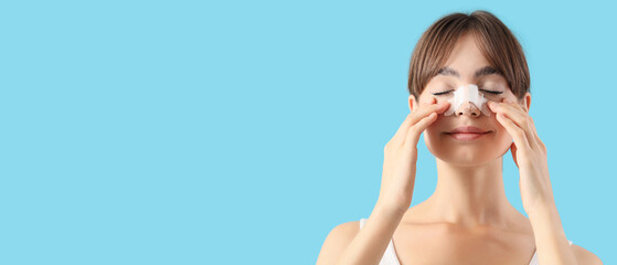 Beautiful young happy woman with bandaged nose on blue background. Plastic surgery concept