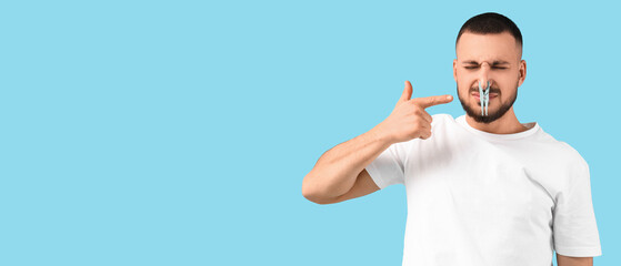 Young man pointing at clothespin on blue background. Stuffy nose concept