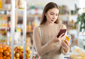 Young woman buyer scanning qr code for yellow smoothie in bottle in grocery store