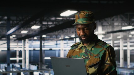 Army IT specialist in data center using laptop to defend networks against cyber threats. Military command center admin using notebook to identify potential intrusions or malicious activities