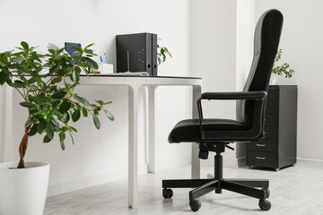 Comfortable workplace with leather black chair near white wall in room, closeup