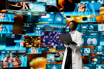 Biomedical specialist wearing lab coat studying pathogens using laptop to design antiviral strategies. African American woman looking at genomes on notebook screen, comparing infection models