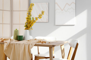 Vase with blooming branches, cup and teapot on table in dining room, closeup