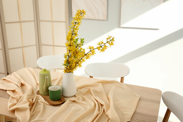 Vase with blooming branches, cup and teapot on table in dining room, closeup