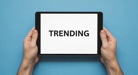 Hands holding a tablet with the word trending displayed on the screen against a blue background color