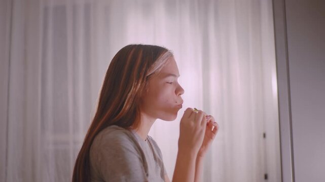 Side view of lady savoring sausage roll with eyes closed in enjoyment, hands holding pastry delicately, warm indoor light highlighting peaceful moment of eating snack reflecting comfort