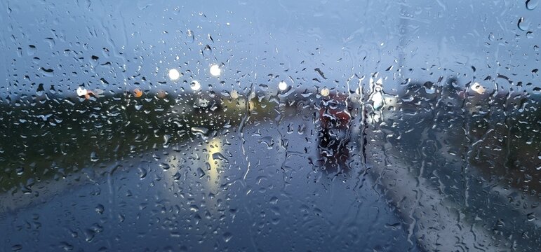 View of a road through a car window during rain with raindrops on the glass