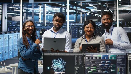 Portrait of smiling data center specialists collaborating in server facility, using node tree...