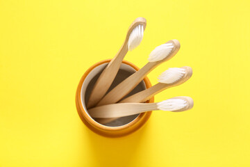 Glass with wooden toothbrushes on yellow background, closeup