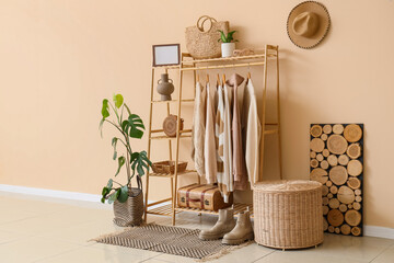 Table, wooden rack with stylish clothes and accessories near beige wall in interior of room