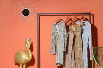 Rack with stylish clothes and golden decorative flamingo near orange wall in room, closeup