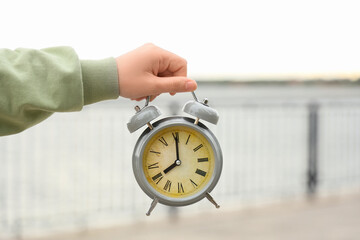Female hand with grey alarm clock outdoors, closeup