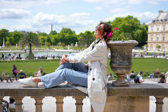 Happy woman in sunglasses relaxing on balustrade with view of Luxembourg Gardens Paris France on sunny day