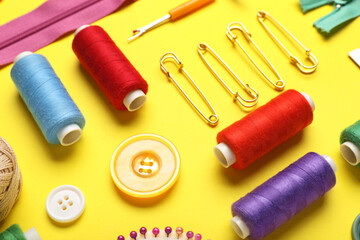 Composition with different thread spools, buttons and pins on yellow background, closeup