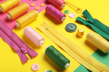Composition with thread spools, zippers and buttons on color background, closeup