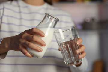 Young woman pouring milk into glass in kitchen at night, closeup