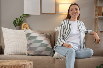 Obraz premium Dreamy young woman sitting on sofa at home