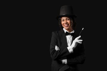 Young African-American magician with magic wand on black background