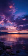 A serene lakeside sunset, showcasing a vibrant purple and orange sky reflected in calm waters. Dark clouds contrast with the warm hues, creating a dramatic yet peaceful scene.  Rocks line the shore