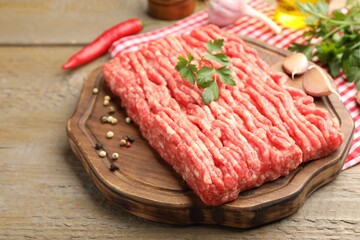 Raw minced meat with parsley and spices on wooden table, closeup