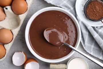 Raw chocolate dough in bowl and ingredients on grey table, flat lay