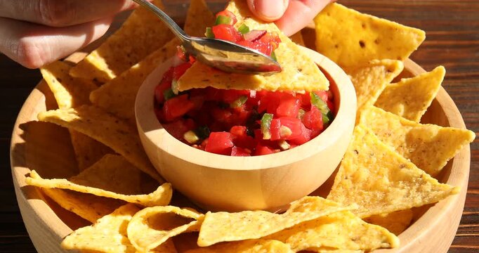 Woman eating nachos with salsa at wooden table, closeup