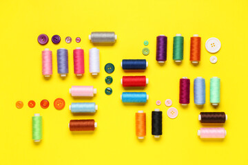Composition with many different thread spools and buttons on yellow background
