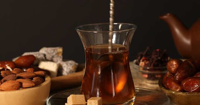 Adding and stirring sugar in glass with Turkish tea at table, closeup