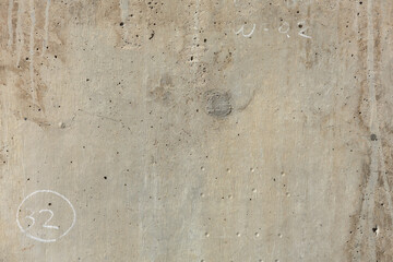 Rough brutalist surface of concrete pillar with air pockets, drilling marks, fine cracks, natural stains, and numerical and alphabetical chalk markings.