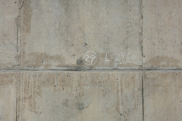 Raw, weathered concrete wall features construction remnants of chalk markings scribbled randomly...