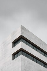 Low-angle shot of a modern, light-grey concrete building corner, featuring horizontal lines of rectangular windows against a muted sky