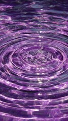 Vibrant purple liquid ripples outward from a central point, creating concentric circles with glistening highlights and subtle texture