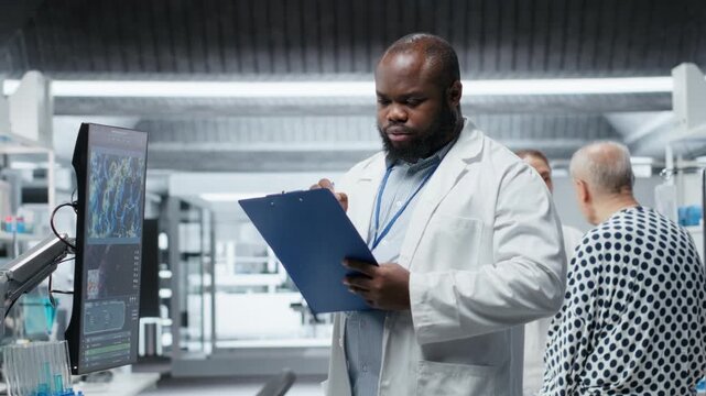 Black medic monitoring patient vitals and DNA molecules on monitor, conducting a laboratory study and testing new treatment. Male doctor works on a medical breakthrough. Camera B.