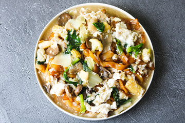 A serving of Kwetiau Siram, an Indonesian dish featuring broad, flat rice noodles in a thick and savory gravy. The dish is filled with vegetables like cauliflower, baby corn, mushrooms, and egg.