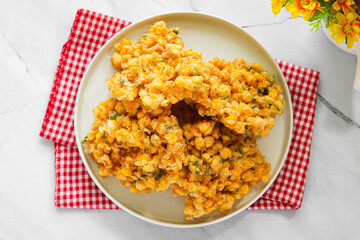A serving of freshly fried Corn Fritters (Bakwan Jagung), golden and crispy, served on a white plate with a checkered cloth.