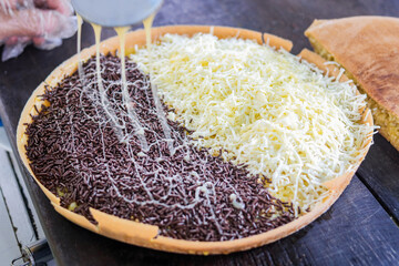 Close-up on a freshly made Martabak Manis (Indonesian sweet pancake). Chocolate sprinkles on one half and shredded cheese on the other. Final touches of condensed milk are drizzled over the top.