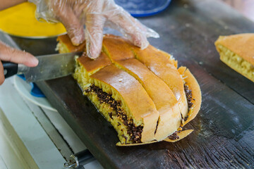 A vendor's gloved hand expertly slices a freshly made Martabak Manis (Indonesian sweet pancake). Chocolate sprinkles on one half and shredded cheese on the other. Bought at a street food vendor.