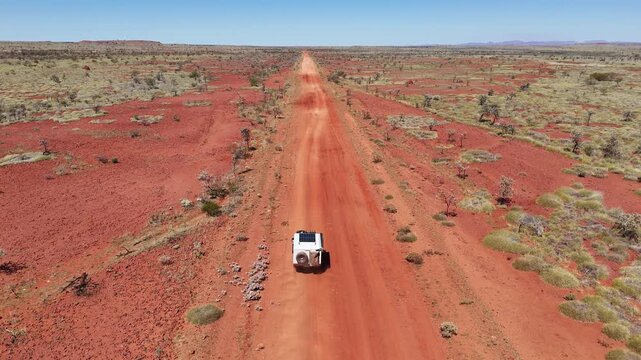 Aerial drone shot 4x4 offroad travel vehicle driving along a red dirt gravel road through the iconic desert of the outback at Karijini national park in the Pilbara, western Australia.