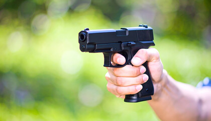 Hand holding black handgun on green background. Suitable for firearm, security, crime and law enforcement related publications or designs.