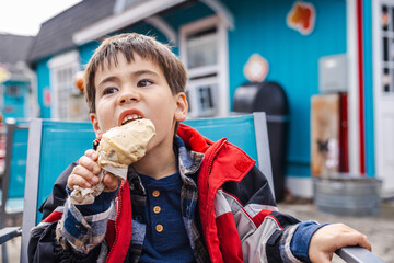 Boy in a red jacket enjoying ice cream outdoors in front of a colorful cafe