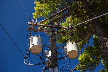 Wooden utility pole with power transformers and electrical cables against blue sky in the United...