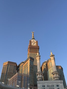 Grand Abraj Al-Bait Clock Tower and surrounding illuminated skyscrapers dominating the skyline in Mecca under a clear blue sky.