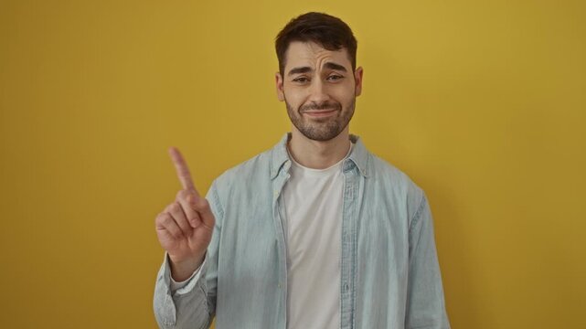 Young man wearing casual shirt gestures no with finger on isolated yellow background, suggesting denial or disagreement.