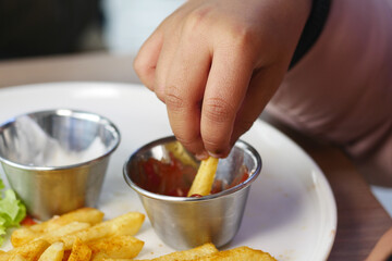 A child hand dips a french fry into a small bowl of ketchup at a restaurant