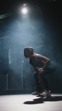 Strong athletic woman lifting kettlebell above head one hand full body view dark gym endurance strength discipline motivation fitness healthy lifestyle vertical slow motion workout