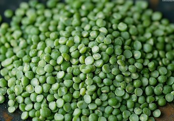 Close-up view of a pile of fresh green split peas scattered on a dark surface, displaying smooth texture and vibrant green color