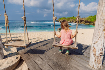 Child girl on swings at beach with blue sea, enjoy childhood