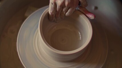 Close-up of hands smoothing inner surface of clay bowl on spinning pottery wheel during ceramics shaping process in art studio